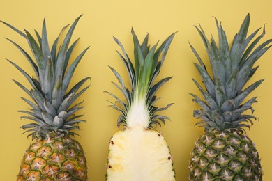 Whole and cut ripe pineapples on yellow background, flat lay