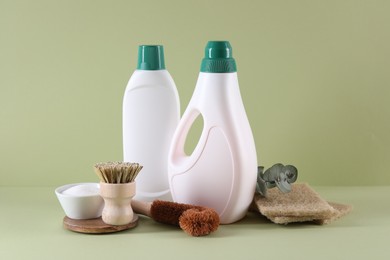 Bottles of cleaning product, sponges, baking soda and brushes on light green background