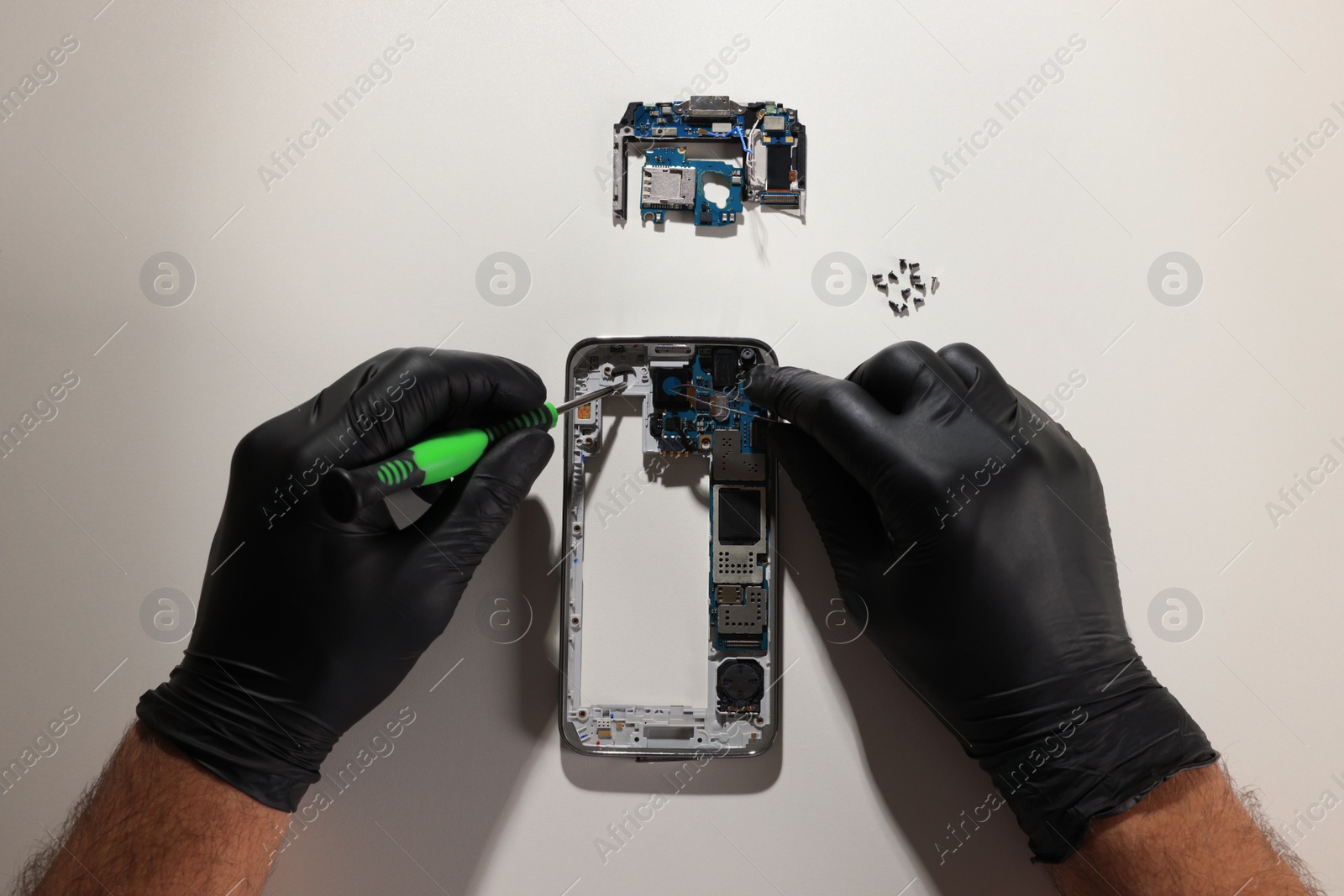 Photo of Technician repairing broken smartphone at white table, top view