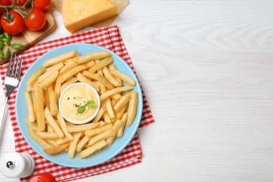 Photo of Delicious French fries and cheese sauce with basil served on white wooden table, flat lay. Space for text