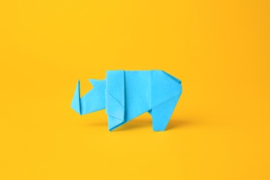 Photo of Origami art. Handmade light blue paper rhinoceros on yellow background