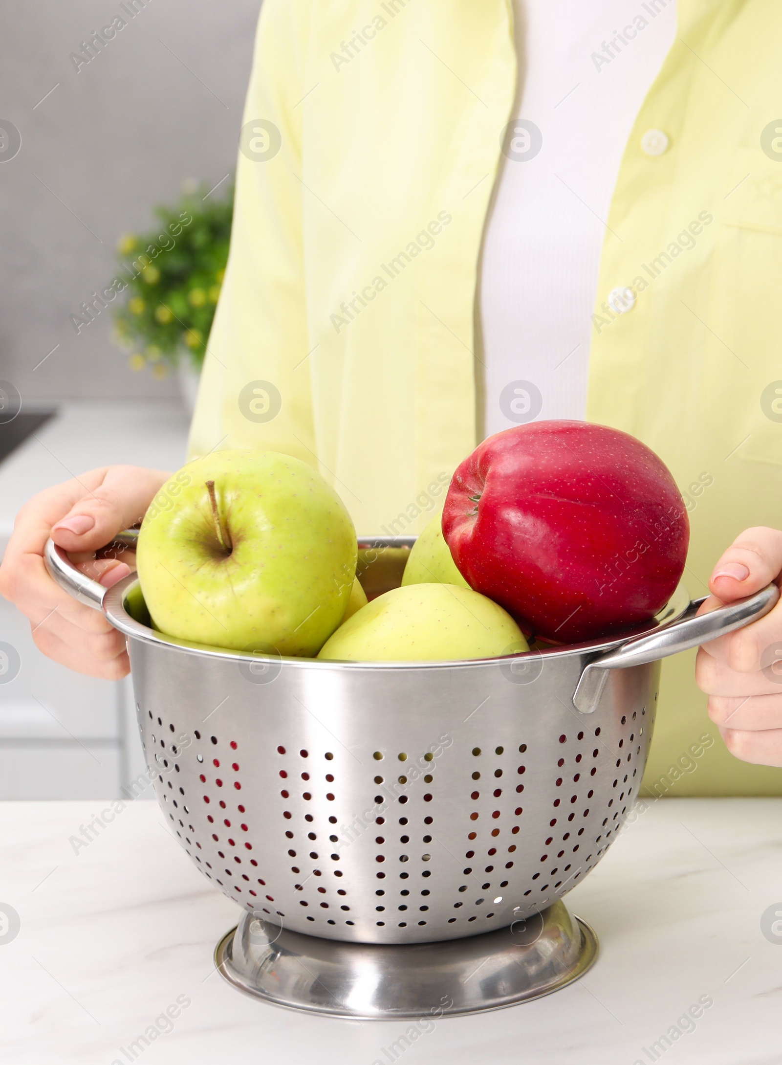 Photo of Woman holding colander with fresh apples at white marble table in kitchen, closeup