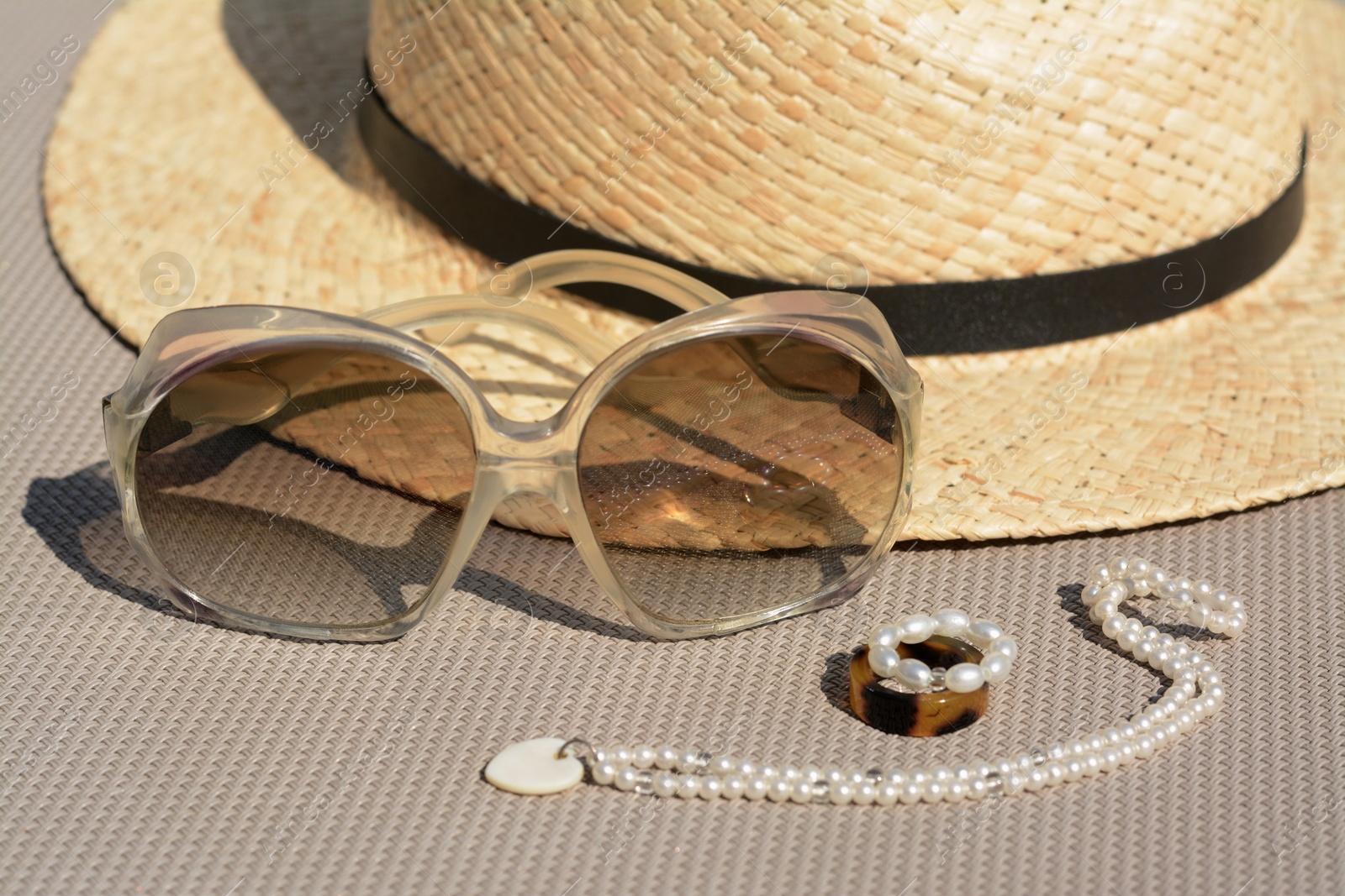 Photo of Stylish hat, sunglasses and jewelry on grey surface, closeup