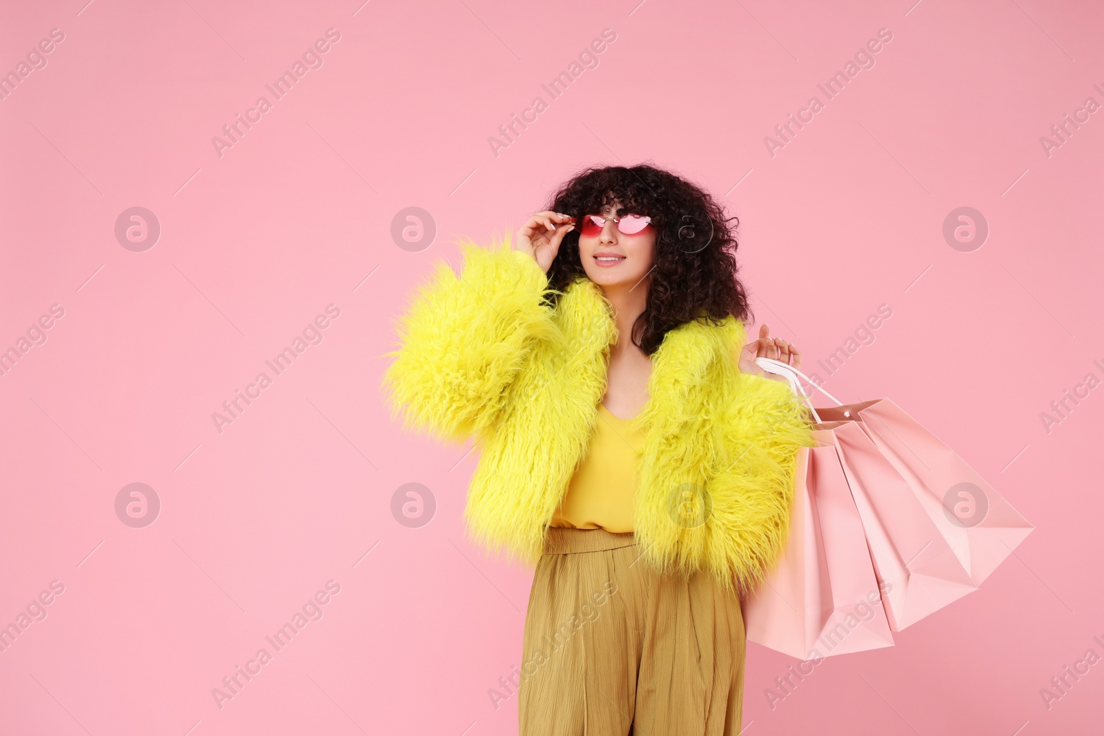 Photo of Happy young woman with shopping bags on pink background. Space for text