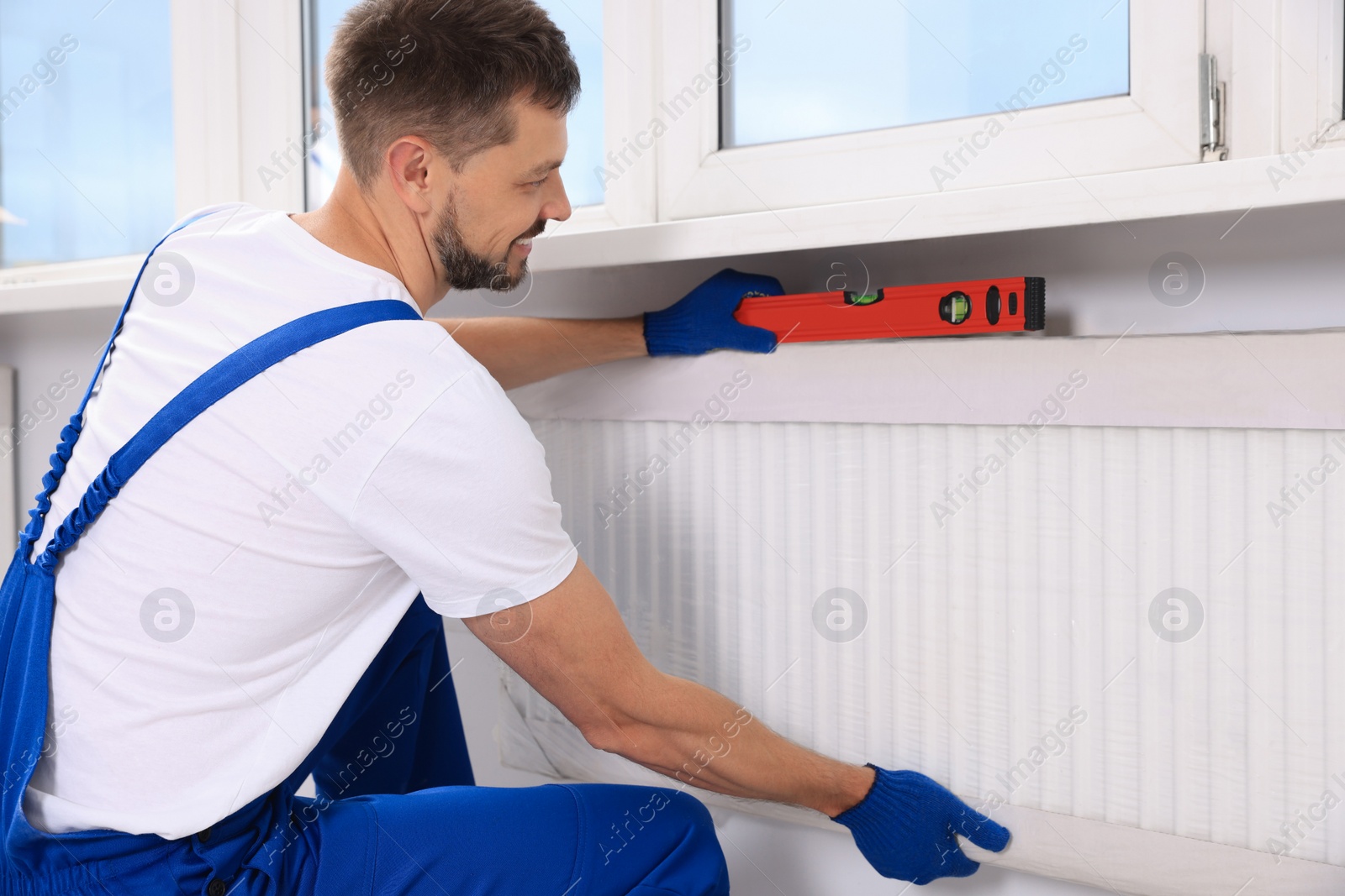 Photo of Professional plumber using bubble level for installing new heating radiator indoors