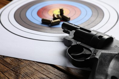 Photo of Shooting target, handgun and bullets on wooden table, closeup