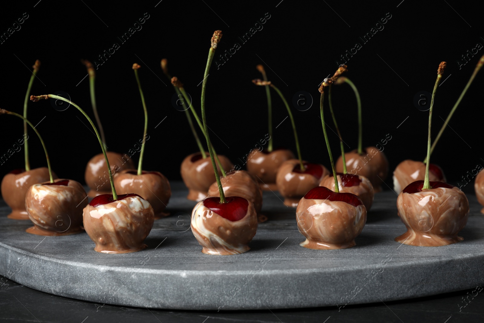 Photo of Sweet chocolate dipped cherries on black table