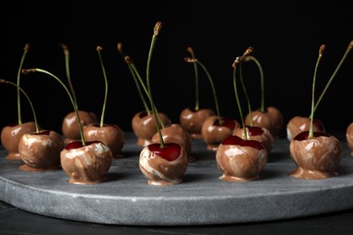 Photo of Sweet chocolate dipped cherries on black table
