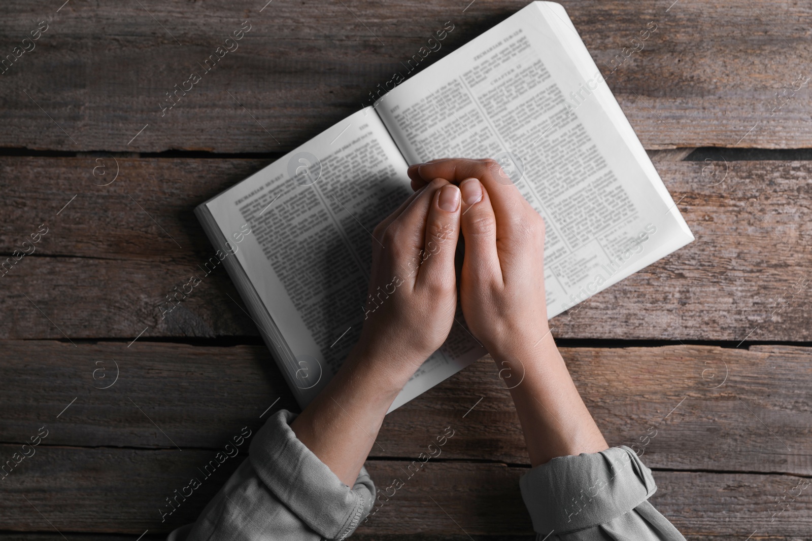 Photo of Religion. Christian woman praying over Bible at wooden table, top view