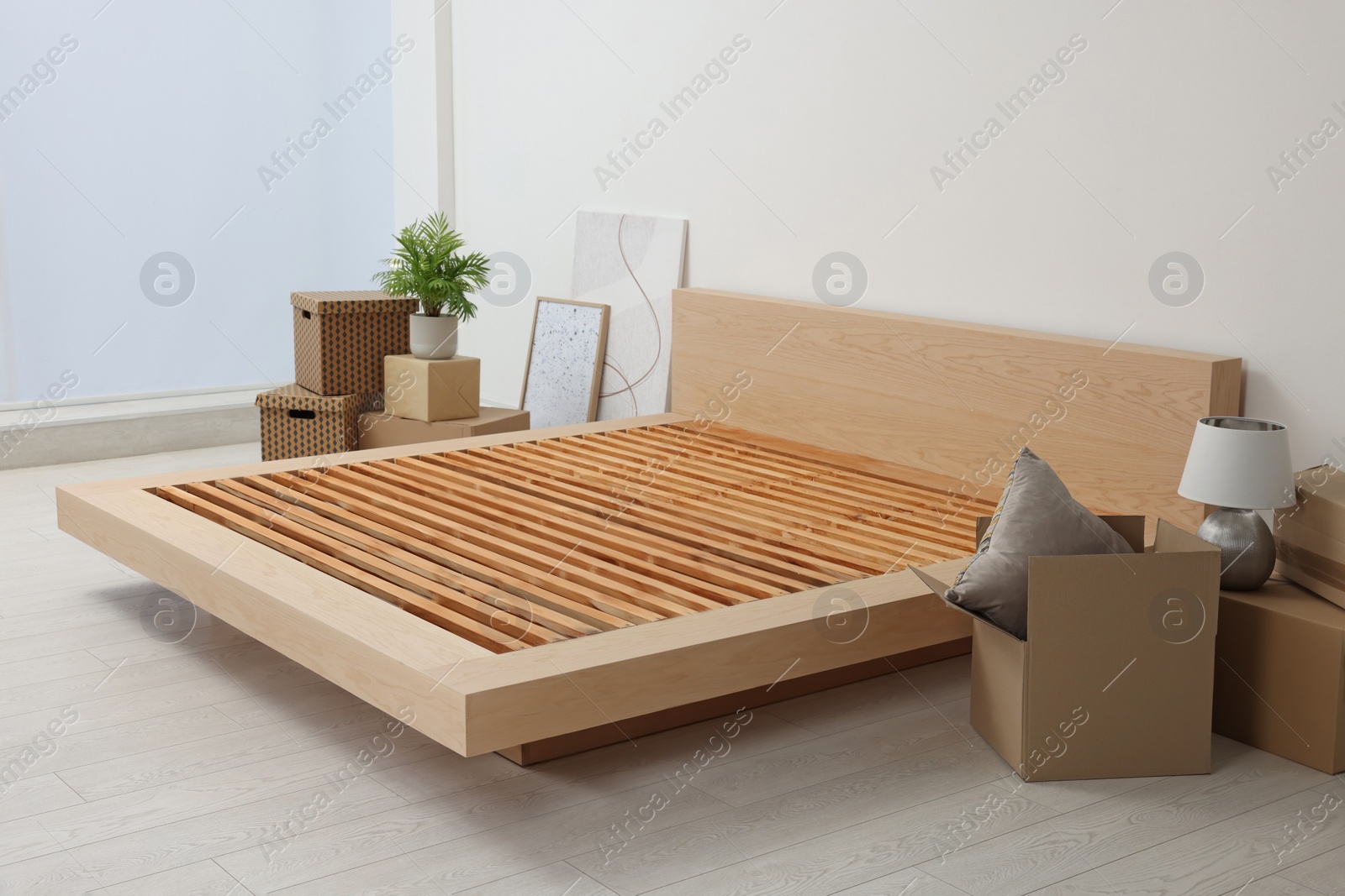 Photo of New wooden bed frame, moving boxes and decor elements indoors