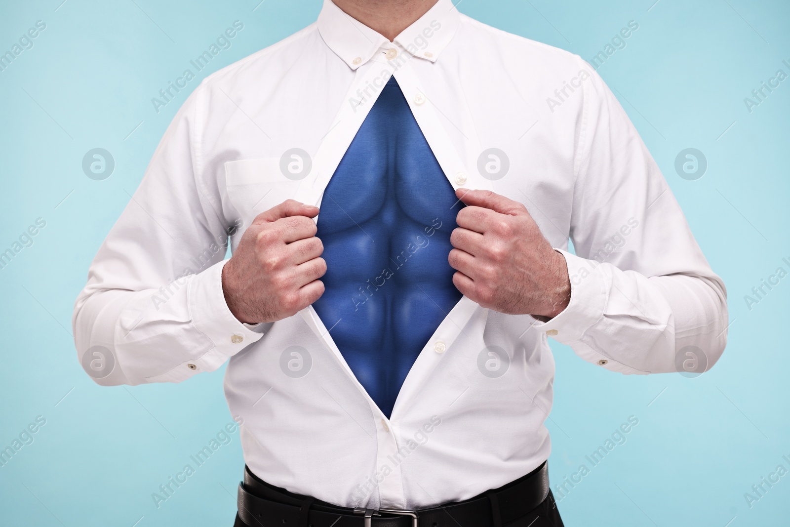 Image of Businessman wearing superhero costume under suit on light blue background, closeup