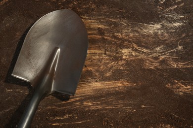 Photo of Metal shovel with fertile soil on dirty wooden surface, top view. Space for text