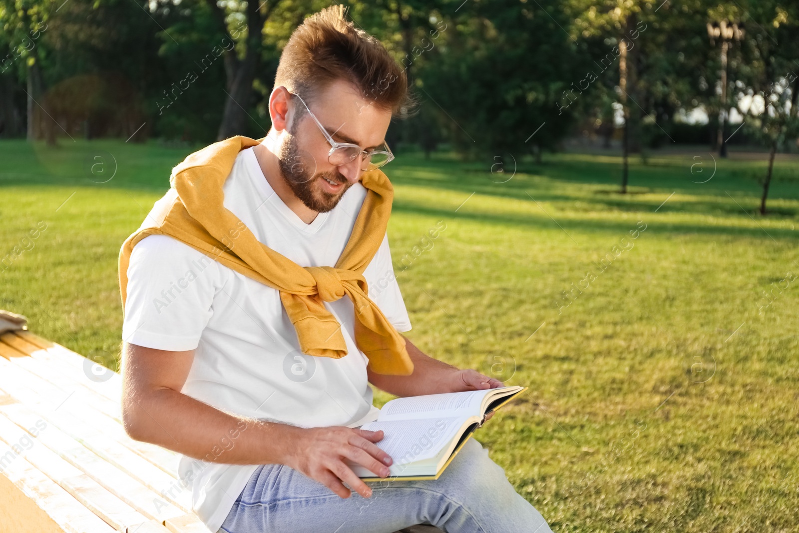 Photo of Young man reading book on bench in park