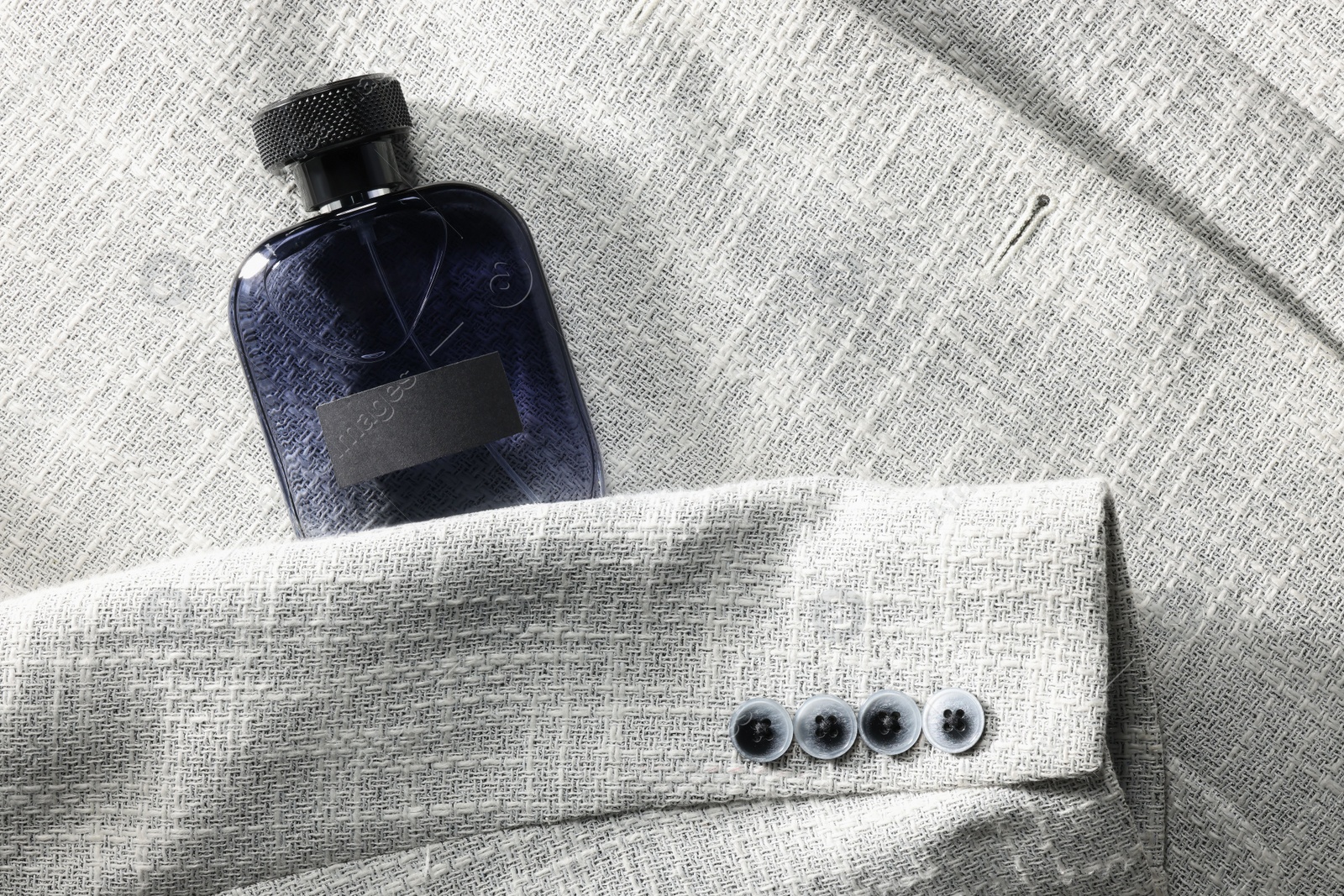 Photo of Luxury men's perfume in bottle on grey jacket, top view. Space for text