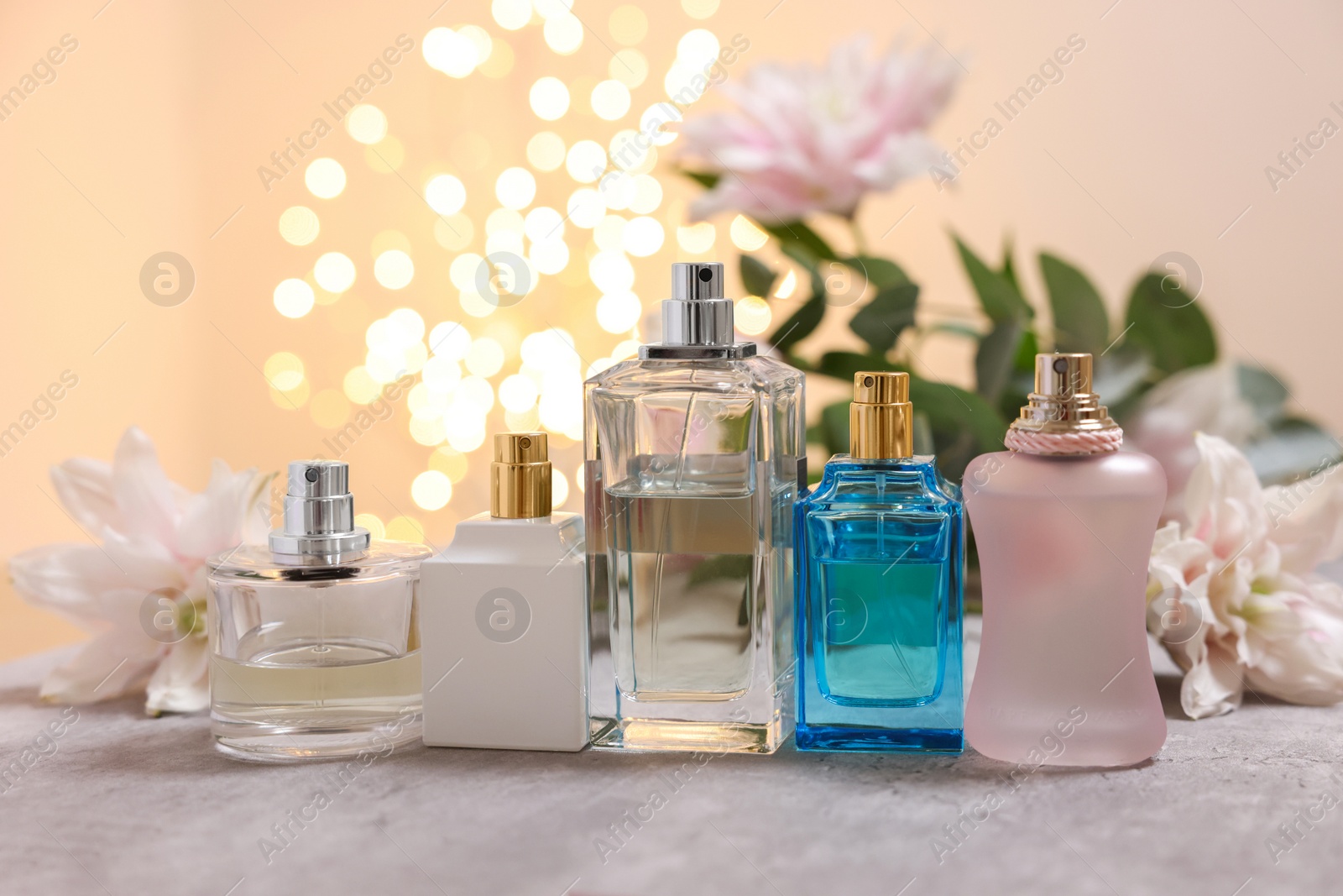 Photo of Perfume bottles and bouquet of beautiful lily flowers on table against beige background with blurred lights, closeup