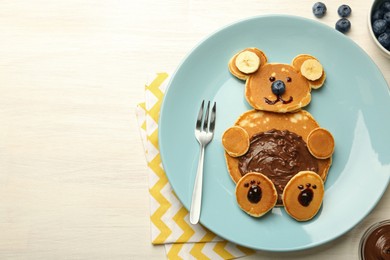 Creative serving for kids. Plate with cute bear made of pancakes, blueberries, bananas and chocolate paste on light wooden table, top view. Space for text