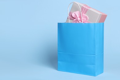 Photo of Bright paper shopping bag with gift box on light blue background. Space for text