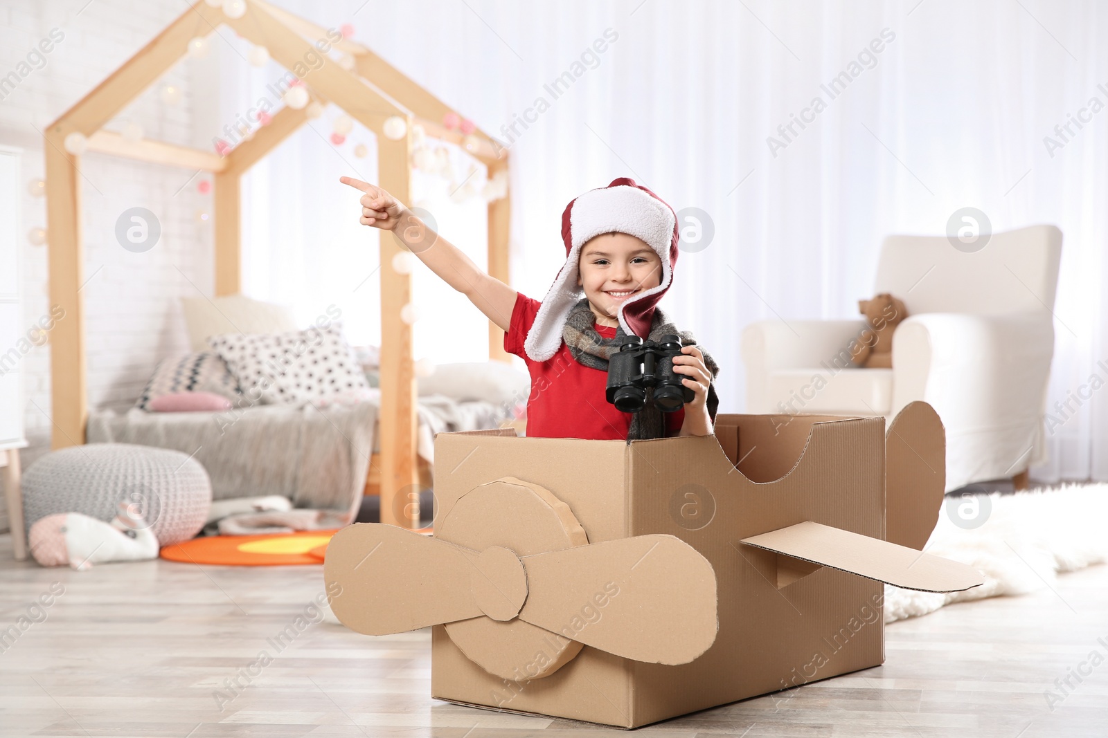 Photo of Cute little boy playing with binoculars and cardboard airplane in bedroom