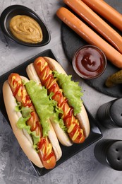 Tasty hot dogs and ingredients on grey textured table, flat lay