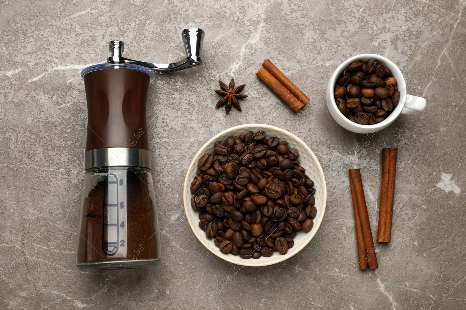 Photo of Manual coffee grinder with powder, beans and cinnamon on grey table, flat lay