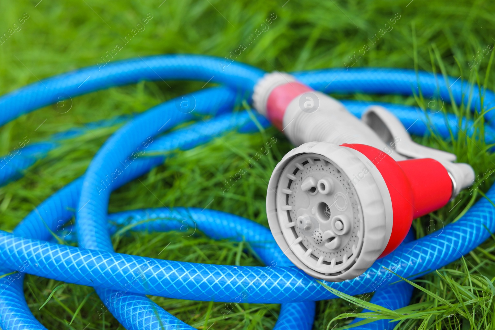 Photo of Watering hose with sprinkler on green grass outdoors, closeup