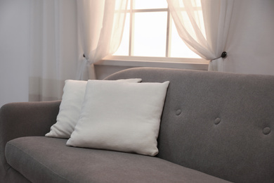 Photo of Modern comfortable sofa with pillows near window indoors. Stylish interior