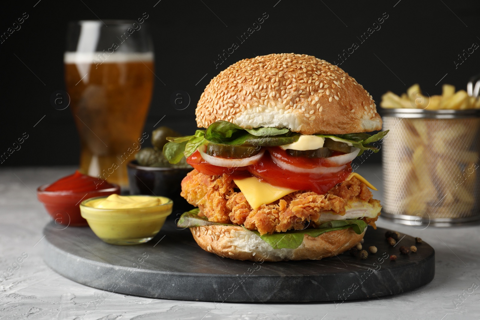 Photo of Delicious burger with crispy chicken patty and sauces on grey table