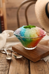 Photo of Rainbow shaving ice in glass dessert bowl on wooden  table indoors