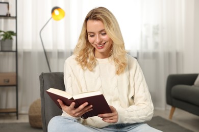 Photo of Happy woman in stylish warm sweater reading book at home