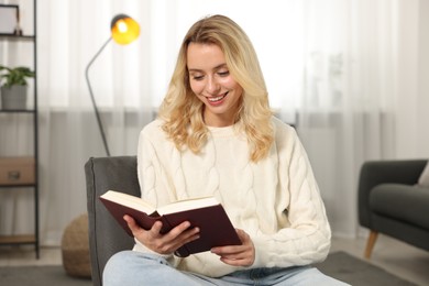 Happy woman in stylish warm sweater reading book at home