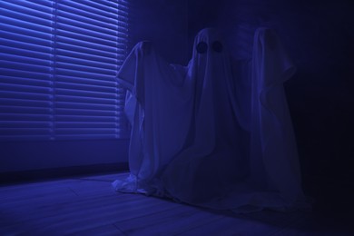 Photo of Creepy ghost. Woman covered with sheet near window in blue light, space for text