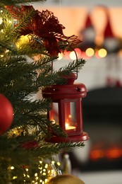 Christmas lantern with burning candle on fir tree indoors, closeup