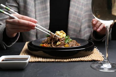 Photo of Stir-fry. Woman eating tasty noodles with meat and vegetables at dark textured table, closeup