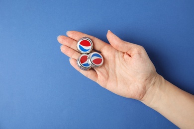 MYKOLAIV, UKRAINE - FEBRUARY 12, 2021: Woman holding Pepsi lids on blue background, top view