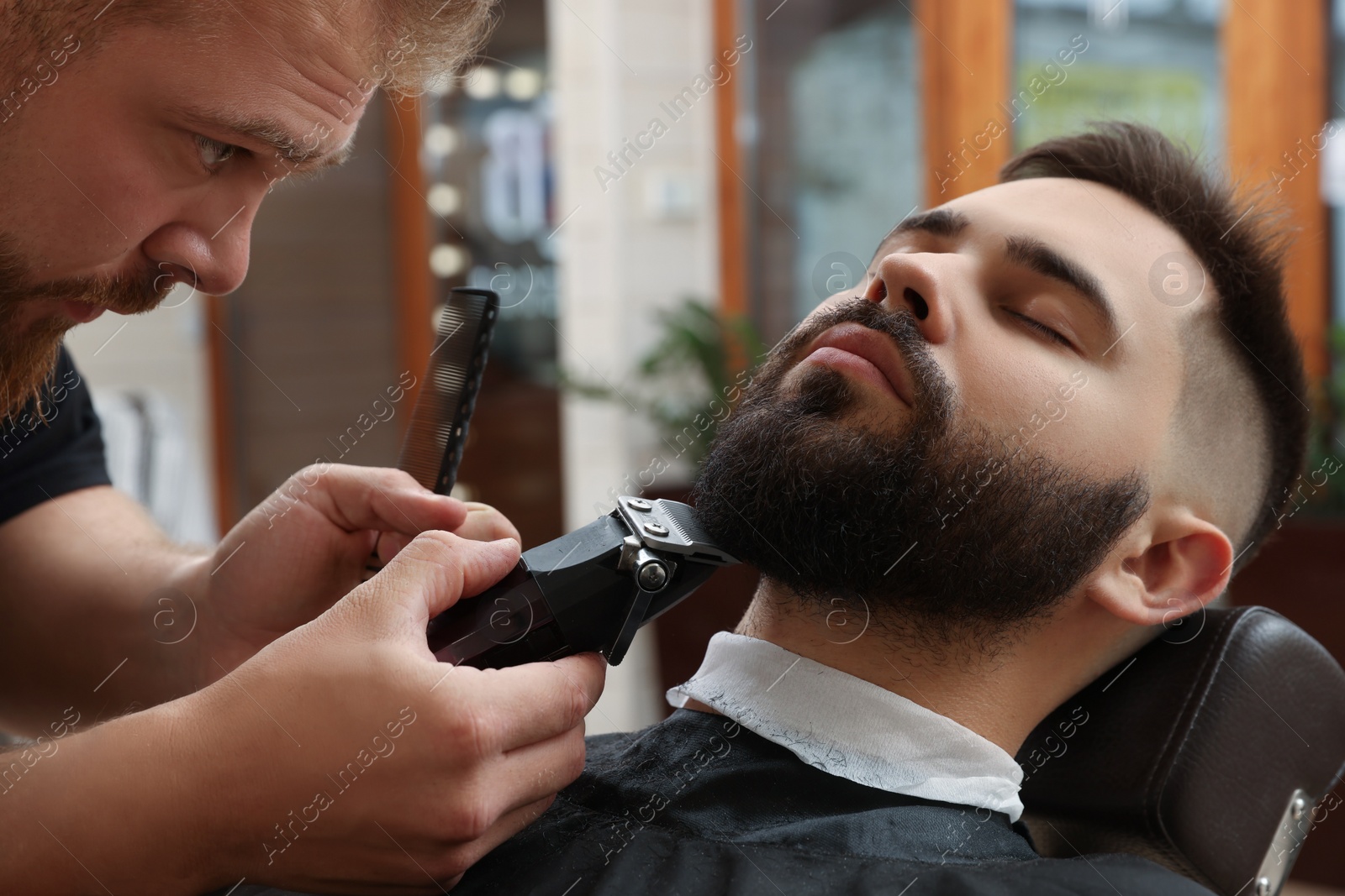 Photo of Professional hairdresser working with client in barbershop, closeup