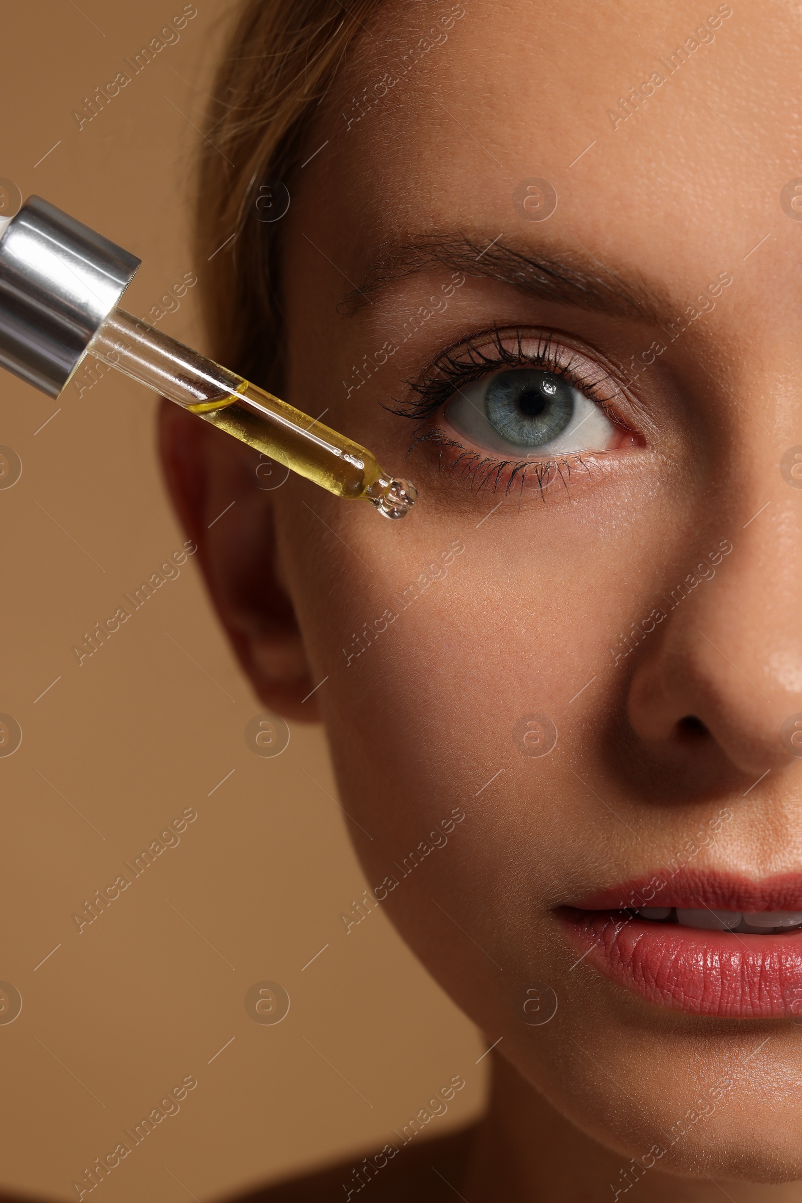 Photo of Woman applying cosmetic serum onto her face on beige background, closeup