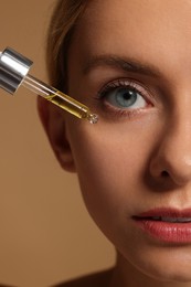 Woman applying cosmetic serum onto her face on beige background, closeup