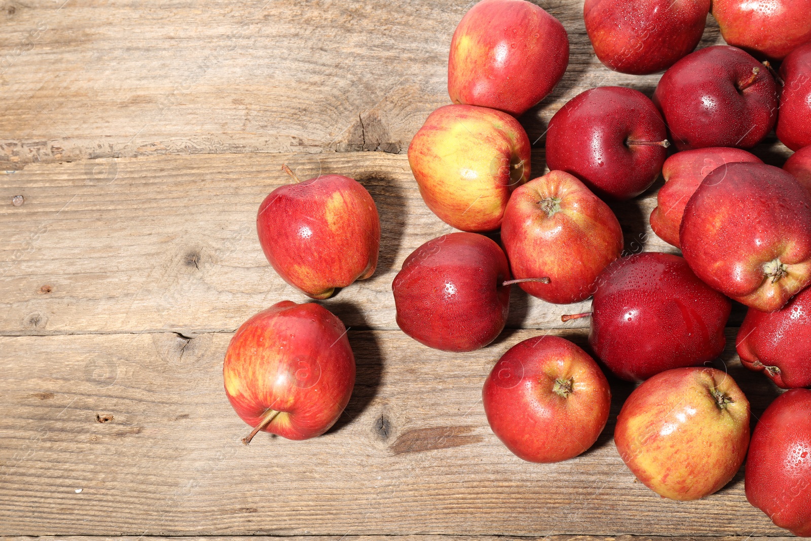 Photo of Many fresh apples with water drops on wooden table, top view. Space for text