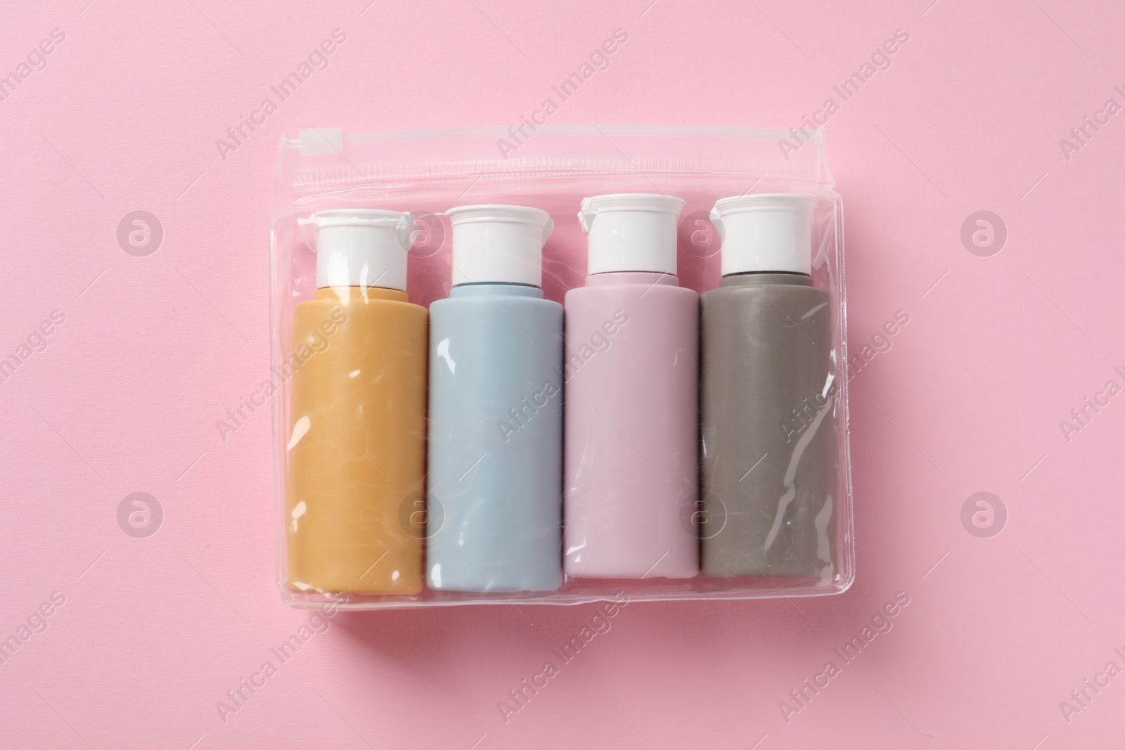 Photo of Cosmetic travel kit in plastic bag on pink background, top view. Bath accessories