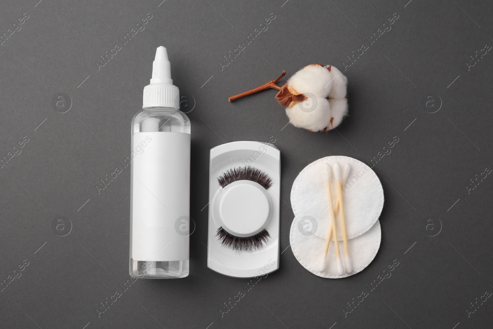 Photo of Bottle of makeup remover, cotton flower, pads, swabs and false eyelashes on grey background, flat lay