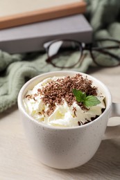 Cup of delicious hot chocolate with whipped cream and mint on white wooden table