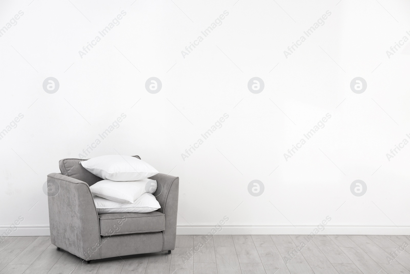 Photo of Pile of soft bed pillows on armchair near white wall with space for text