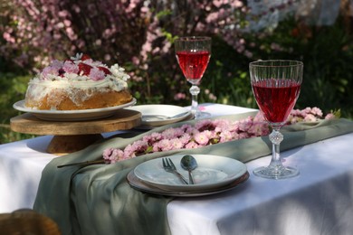 Beautiful spring flowers, delicious cake and wine glasses on table in garden