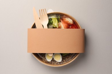 Tasty food in container with wooden fork and knife on light background, top view. Space for text