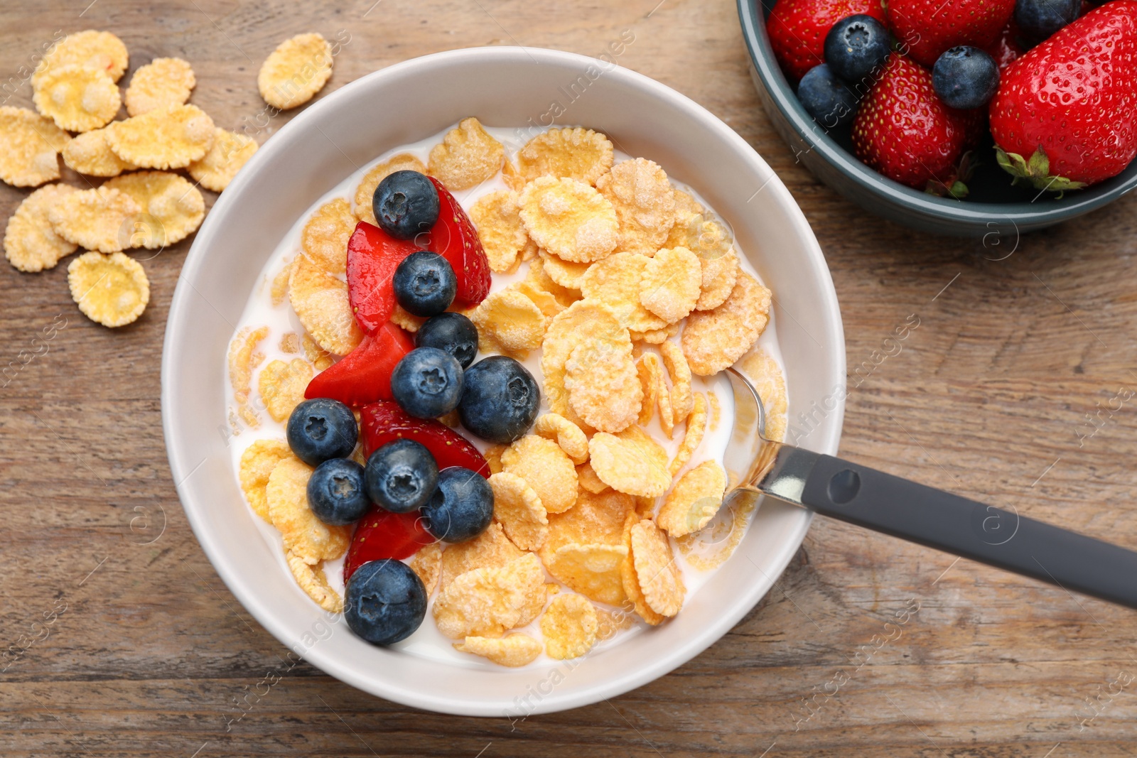 Photo of Bowl of tasty crispy corn flakes with milk and berries on wooden table, flat lay