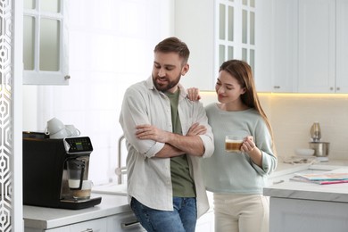 Young man and his girlfriend using modern coffee machine in kitchen