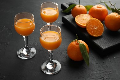 Photo of Tasty tangerine liqueur in glasses and fresh citrus fruits on black textured table