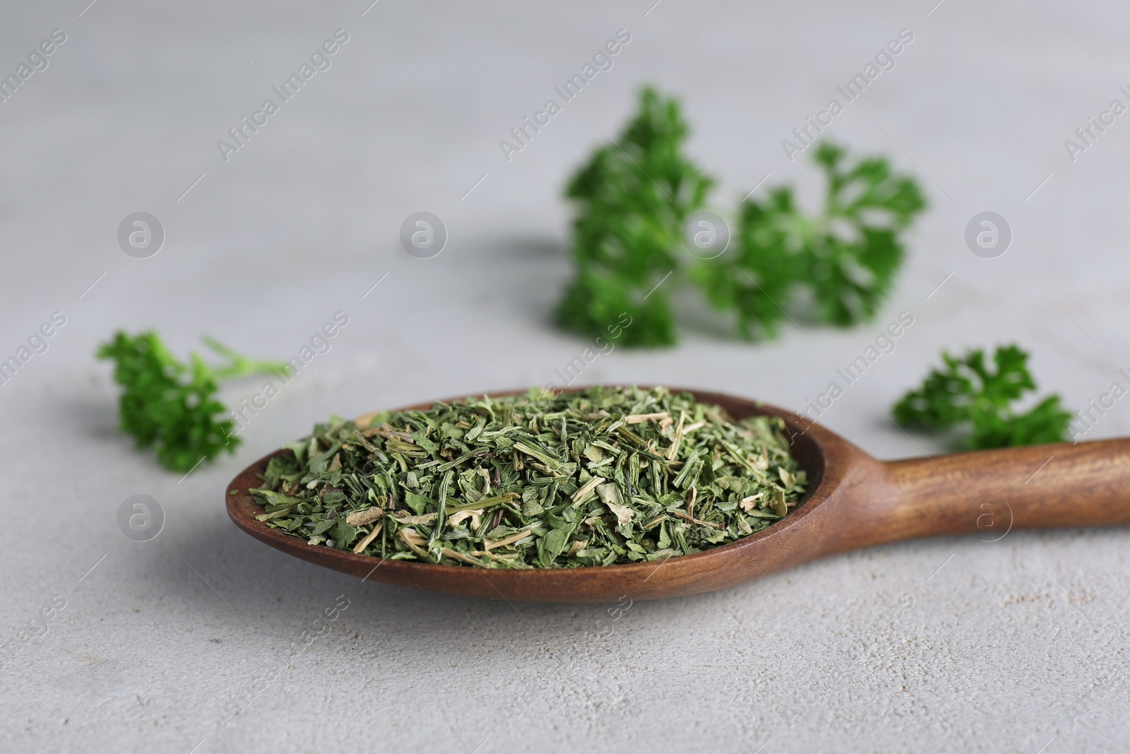 Photo of Spoon with dry parsley on grey table