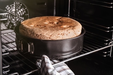 Person taking delicious fresh homemade cake from oven, closeup