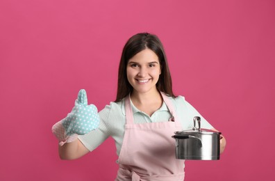 Happy young woman with cooking pot on pink background